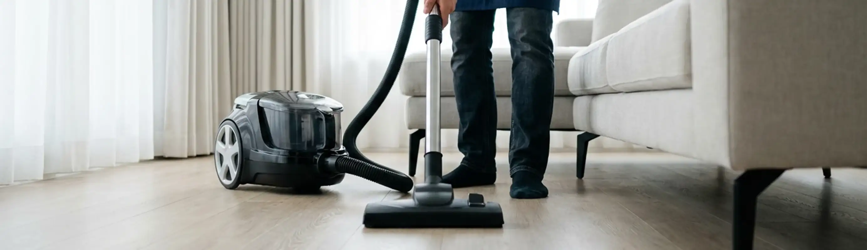 Professional house cleaner vacuuming a living room floor with a canister vacuum cleaner, Jersey City, NJ.