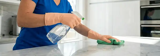 Maid service worker spraying and wiping a kitchen countertop with a microfiber cloth for sanitizing, Jersey City, NJ.