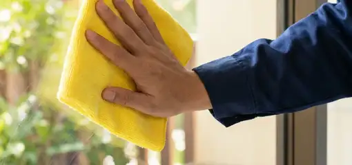 House cleaner wiping a glass window with a yellow microfiber cloth for streak-free cleaning, Jersey City, NJ.